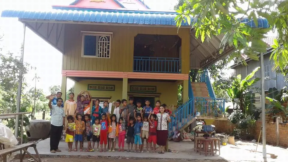 Children and adults gathered in front of a raised house at Kampong Dey Dos, Cambodia
