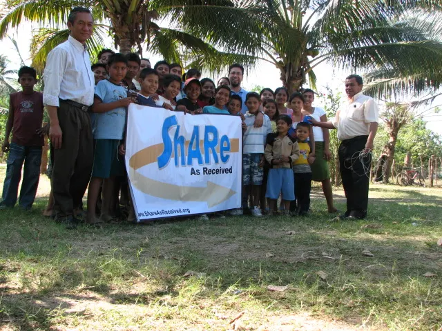 Children and adults holding a ShARe banner under palm trees in Puerto Nuevo