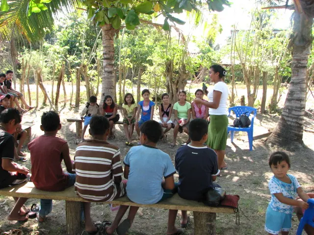 Children on wooden benches listening to a teacher outdoors in Puerto Nuevo, El Salvador